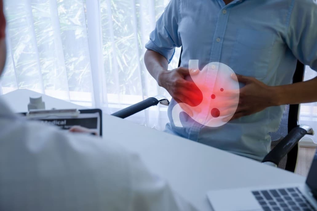 Hombre con dolor abdominal mientras sostiene su estómago, acompañado de una ilustración gráfica que muestra inflamación o irritación gástrica.