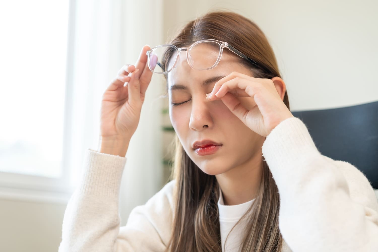 Una mujer joven con anteojos que muestra molestias en los ojos.