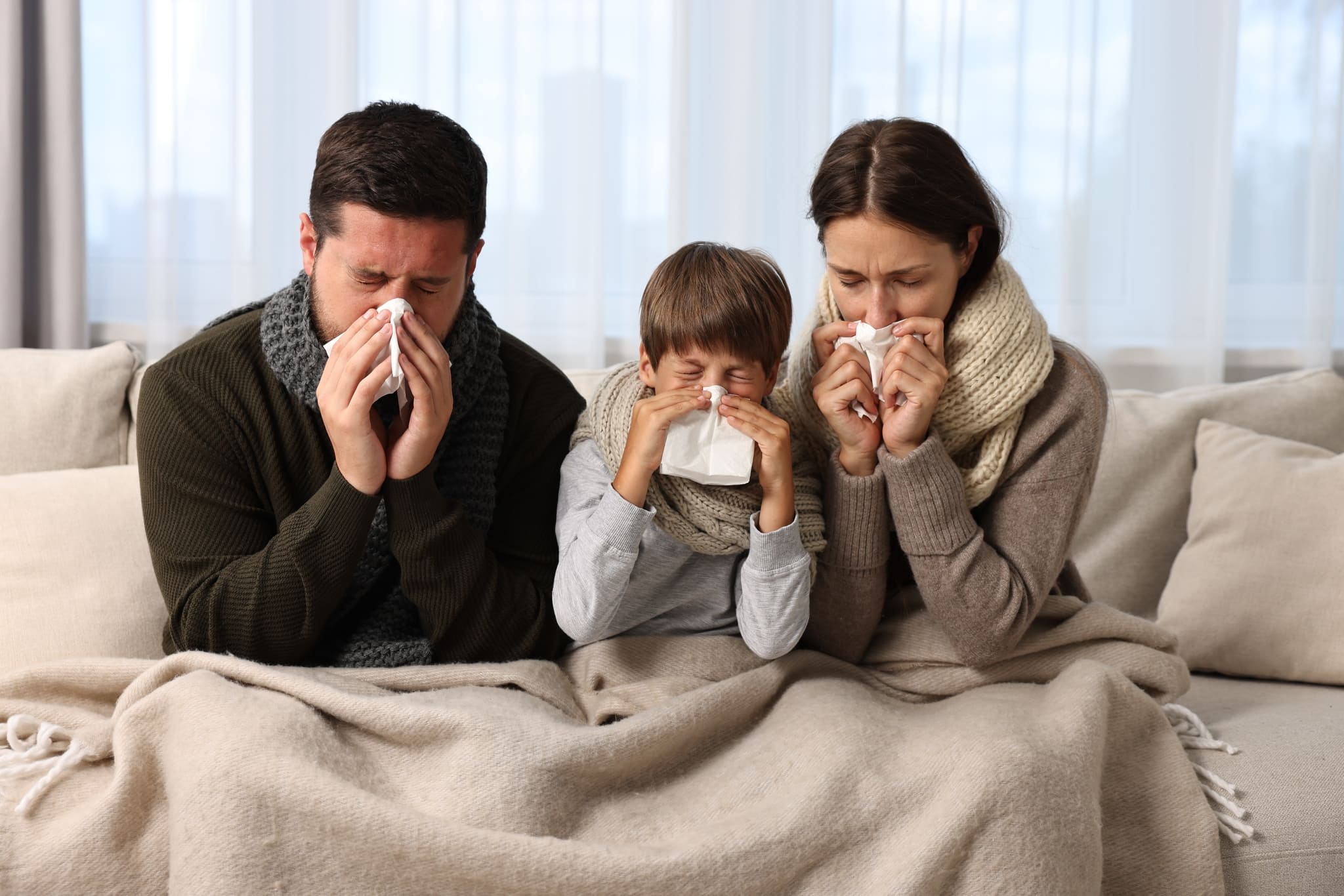 Familia engripada sentados en el sofá, con claros rasgos de influenza.