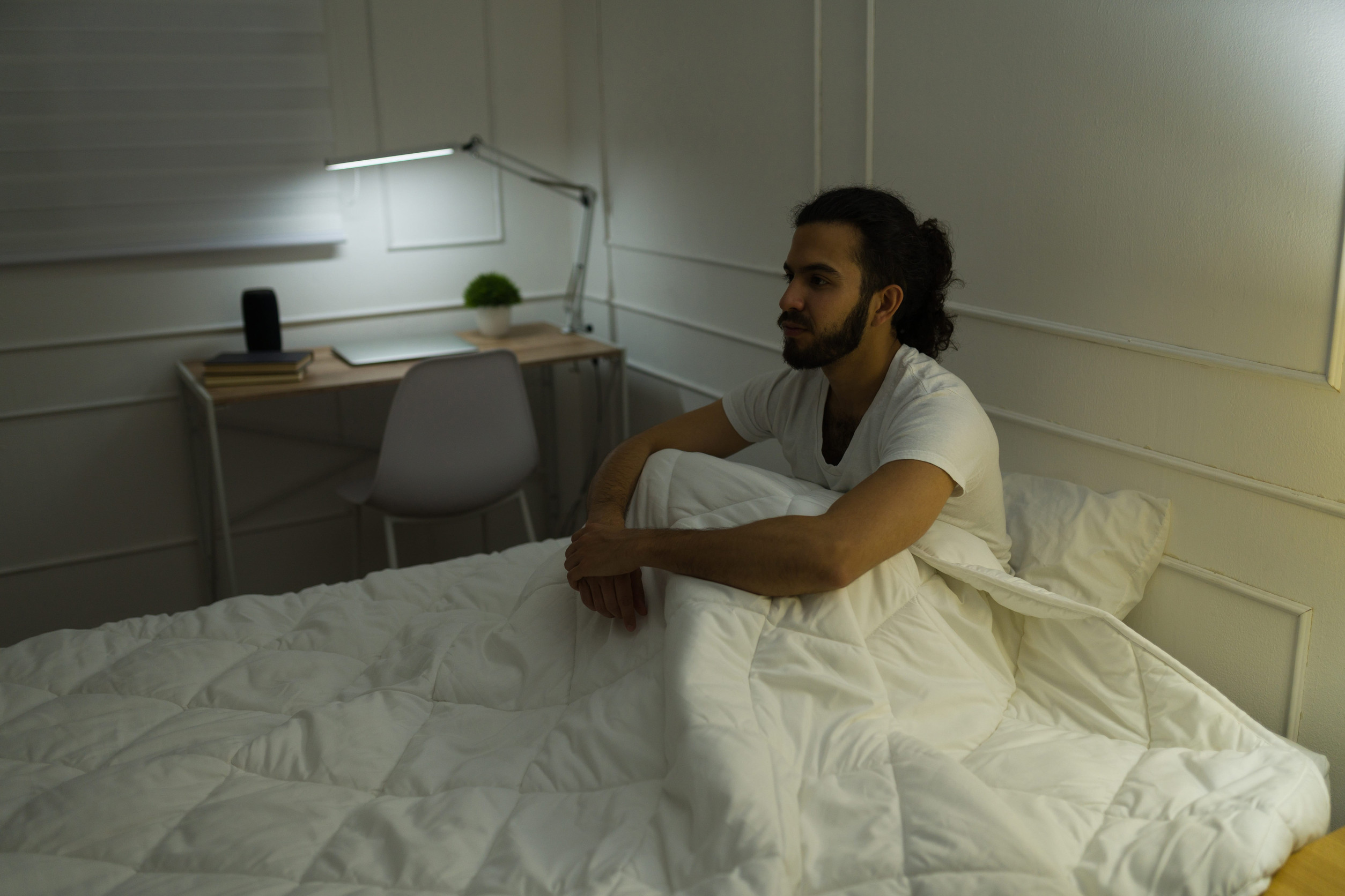 Hombre joven sentado en la cama sin poder dormir.