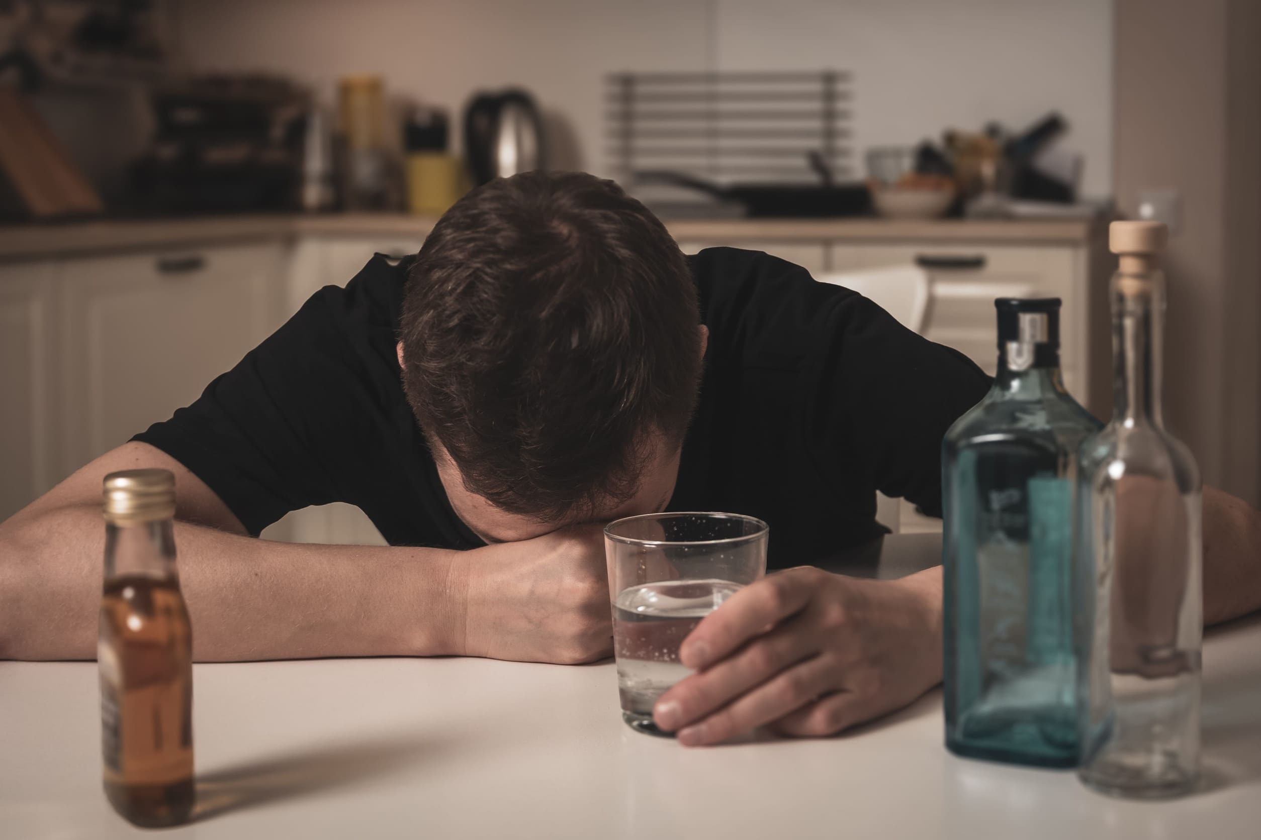 Hombre con un vaso de alcohol y otras botellas