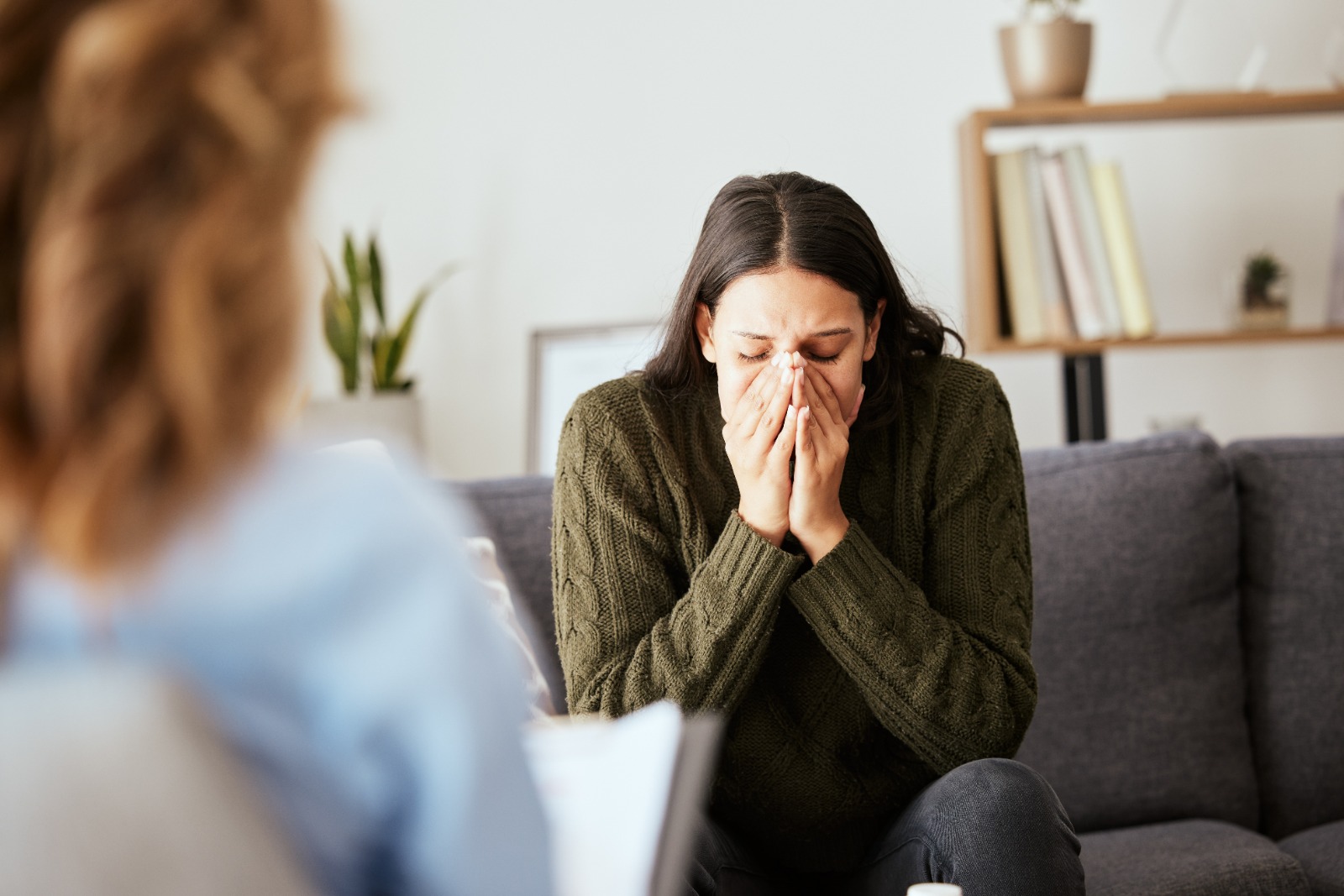 Mujer joven en sesión de terapia, cubriéndose el rostro con las manos y mostrando signos de angustia emocional o ansiedad
