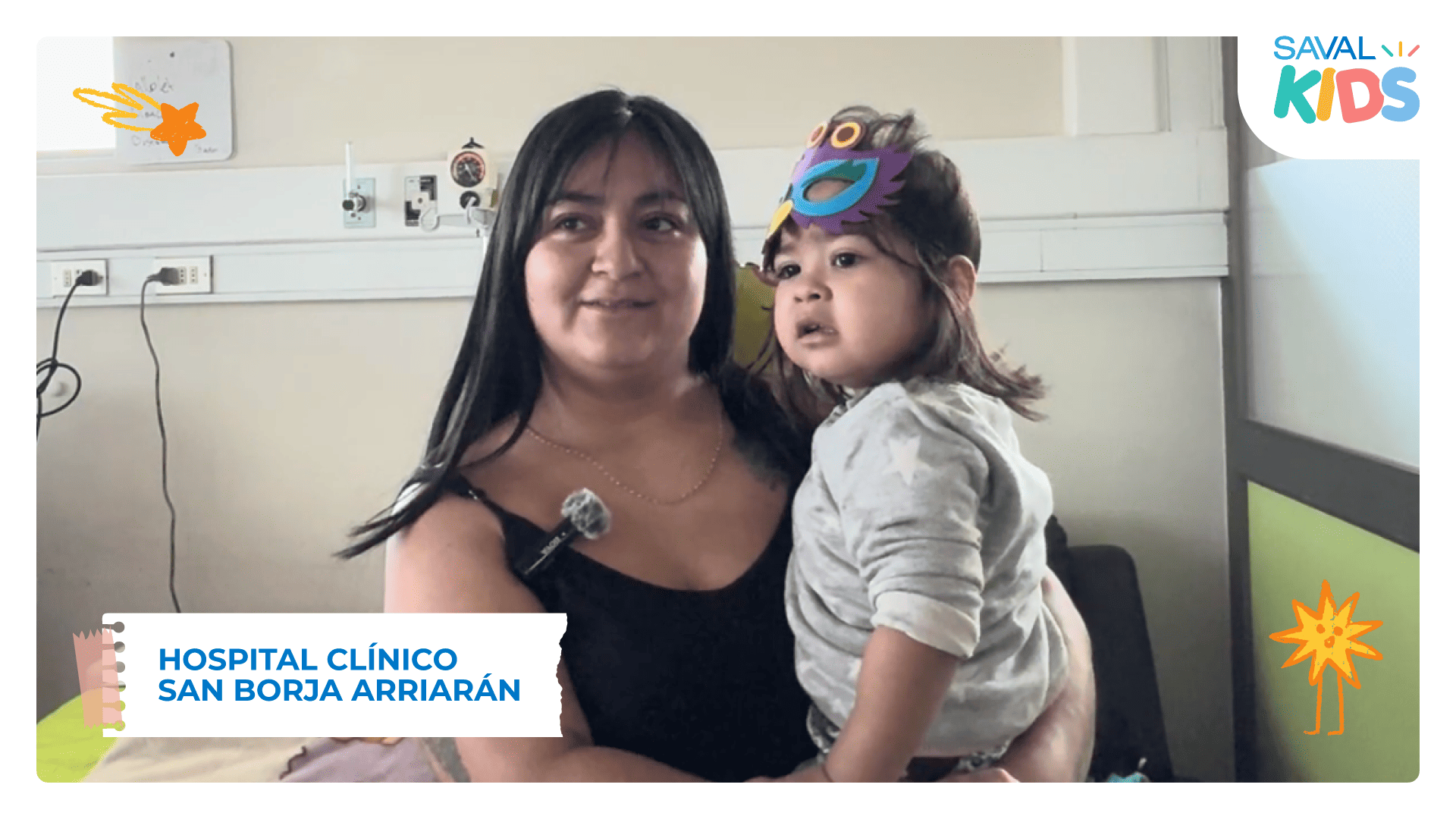 Una madre sostiene en brazos a su hija, que lleva una máscara decorada, en una habitación del Hospital San Borja Arriarán durante SAVAL Kids.